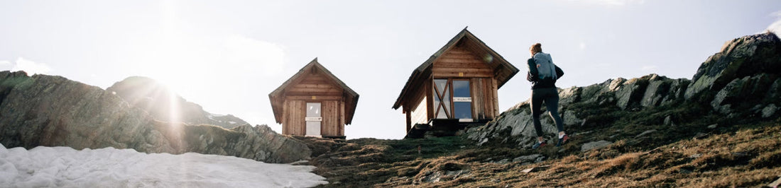 Person hiking towards wooden cabins with a tactical backpack, learning how to choose a tactical backpack.