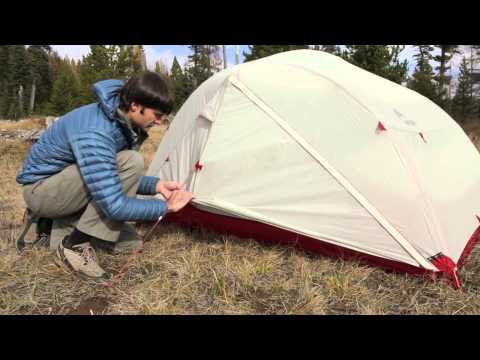 MSR Mutha Hubba NX three-person tent set up outdoors with a person adjusting the entrance in nature